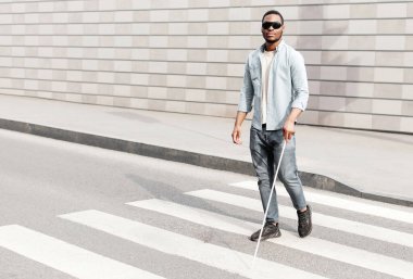 Tam boy, görme engelli, siyah gözlüklü, şehir merkezinde caddenin karşısına geçmek için baston kullanan siyahi bir adam. Engelleme ve kentsel yaşam tarzı kavramı