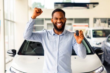 Kendi araban. Afro-Amerikan Adam Otomobil Anahtarı Tutuyor ve Satış Merkezinde beklerken Heyecandan Yumruk Sallıyor, Mutlu Siyah Adam Satın Alım Aracı, Ücretsiz Alan Kutlaması