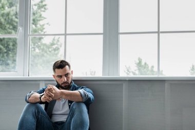 Üzgün, yorgun ve endişeli hisseden bir adam, akıl sağlığı, problemler ve kırık bir kalple depresyon geçiriyor. Hüsrana uğramış genç, yakışıklı sakallı adam büyük pencerenin yanında oturuyor, fotokopi odası, panorama.