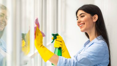 Koruyucu lastik eldivenli güzel bir bayanın portresi. Evde deterjanla pencereyi temizliyor. Sevgili milenyum ev hanımı evini düzenli tutuyor, ev işlerini ve ev işlerini yapıyor.