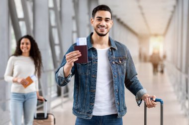 Uçuş rezervasyon servisi. Havalimanında pasaportu ve biletleri olan mutlu bir Arap adam, Orta Doğulu yakışıklı sırıtan bir adam, terminalde uçak beklerken yanında duruyor.