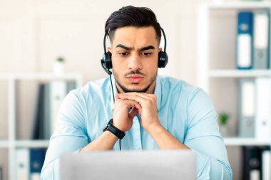 Bin yıllık kulaklıklı endişeli bir Arap iş ortağıyla online video görüşmesi yapıyor, ofisinde sorun yaşıyor. Mutsuz genç Doğulu adam sanal toplantı ya da bilgisayar ekranında konferans yapıyor.