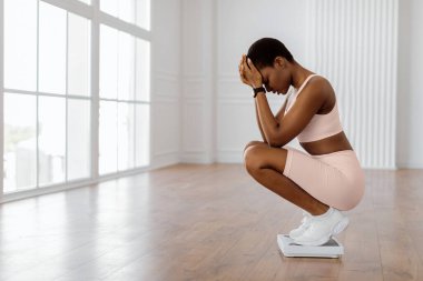 Kilo verme problemleri ve diyet. Üzgün ve hayal kırıklığına uğramış Afrikalı Amerikalı Kadın Banyo Ölçülerini Kullanıyor, Vücut Parametrelerinden Mutsuz, Kafasını Tutan. Boş Kopyalama Alanı, Bulanık Arkaplan