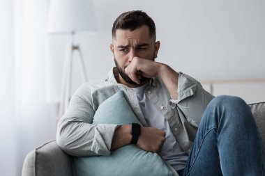 Olumsuz duyguların ifadesi, stres, depresyon, acı ve psikolojik sorunlar. Heyecanlı genç adam yastıkla kanepede oturur, yüzü elle kaplanır ve oturma odasında ağlar.