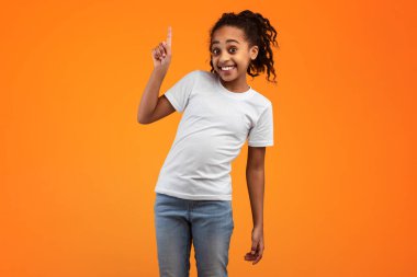 Şuraya bak. Kafasının üstünde parmağıyla işaret eden gülümseyen Afrikalı Amerikalı kızın portresi turuncu sarı stüdyo arka planında duruyor ve bilgilerinizi sunuyor. Bir Numara İşareti