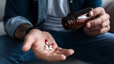 Erkek hastaların avuçlarında bir avuç dolusu beyaz hap. Sağlık, tedavi, uyuşturucu ve depresyon, acı ve intihar. Hüsrana uğramış üzgün genç adam evde antidepresanları elinde tutuyor. Kapatın, kırpın.