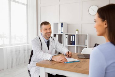 Ziyaret kliniği. Hastanedeki randevusu sırasında, deneyimli orta yaşlı bir tıp hekiminin portresi, yazılar. Gülümseyen doktor ofisinde bir kadınla oturuyor.