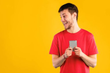 Pozitif meraklı adamın portresi, cep telefonu tutan, mavi stüdyo arka planında tek başına duran, yana bakan, gözetleyen ve bir şeyler görmeye çalışan, cihaz kullanan, boş alan. İnternette sohbet eden adam.