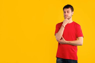 Düşünceli komik adamın portresi soru sormayı düşünüyor, çeneye dokunuyor ve fotokopi alanına bakıyor, fikri düşünüyor. Mavi stüdyo arka planında tek başına duran genç adam.