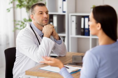 Doktor randevusu. Kadın hasta pratisyen hekimle konuşuyor, belirtileri açıklıyor. Modern ofisinde masa başında oturan bir kadına danışmanlık yapan bir uzman.