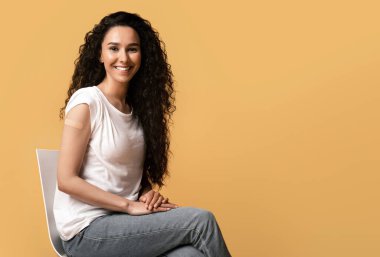 Aşı kavramından sonra. Coronavirus aşısından sonra kollarını gösteren güzel bir Arap kadının portresi, sarı arka planda kolları kıvrılmış, sırıtan esmer bir kadın.