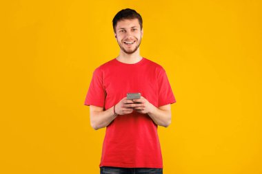 Halk ve Teknoloji Konsepti. Mavi stüdyo arka planında izole edilmiş akıllı telefon kullanan mutlu genç adam portresi, kopyalama alanı. İnternette sohbet eden, kameraya bakan bir adam.