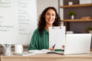 Gülümseyen bayan yöneticinin kameraya bakması, sanal sunum yapması veya öğrencilere online ders vermesi. Web kamerasına belge sözleşmesi gösteren kadın, boş kağıt parçasına işaret ediyor