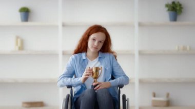 Tekerlekli sandalyede oturan kızıl saçlı bir genç, parlak, minimalist bir odada bir kupa tutuyor. Başarısını vurgulayan tarafsız bir dekorla çevrili düşünceli bir yüz ifadesi sergiliyor..