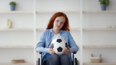 Kızıl saçlı genç bir kız elinde futbol topu tutarken tekerlekli sandalyede oturuyor. Düşünceli ve meşgul görünüyor, meydan okumalarına rağmen spora olan aşkını gösteriyor..