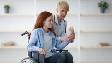 Tekerlekli sandalyedeki kızıl saçlı genç bir kız bakıcısıyla evde iletişim kuruyor. Çevre, faaliyetleri sırasında destekleyici ve dostane bir atmosferi vurgulayan minimalist bir dekor içeriyor..