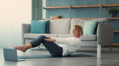 Son sınıf öğrencisi bir kadın evinde egzersiz yapıyor. Sağlığı için azim ve şevk göstererek spor yaparken odaklanmış ve gülümsüyor..