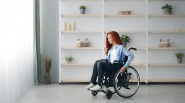 Kızıl saçlı genç bir kız, parlak bir odada, az dekorlu bir tekerlekli sandalyede oturuyor. Etrafında sakin ve meşgul görünüyor, günlük yaşamında gücünü ve bağımsızlığını gösteriyor..