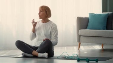 Son sınıf öğrencisi bir kadın yoga minderinde oturur, evde egzersiz yaptıktan sonra biraz dinlenir. Sağlığına ve sağlığına odaklanıyor, sağlıklı bir yaşam tarzını benimsiyor..