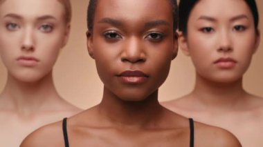 Üç modelden oluşan bir grup yan yana duruyor, farklı ten renkleri ve özellikleri sergiliyorlar. İfadeleri ciddi ve kendinden emin. Moda endüstrisindeki güzellik ve çeşitliliği vurguluyorlar..