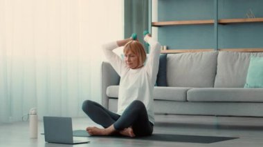 Son sınıf öğrencisi bir kadın evde yoga ya da esneme egzersizleri yapıyor. Dizüstü bilgisayarından talimatları takip ederken spor yapıyor..