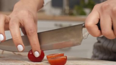 Bir aşçı, mutfak tezgahında keskin bir bıçakla domatesleri dikkatlice ikiye böler..