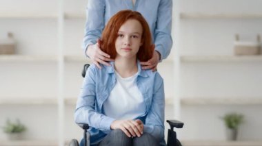 Kızıl saçlı bir genç kız evde tekerlekli sandalyede rahat bir şekilde otururken bir bakıcı onu arkasından nazikçe destekliyor. Çevre sıcak ve davetkar, besleyici bir atmosfer sergiliyor..