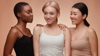 Farklı geçmişlere sahip üç kadın bir arada, gülümsüyor ve sohbet ediyorlar. Yumuşak, sıcak renkli bir arka plana karşı dostluk ve dostluk duyguları sergiliyorlar..