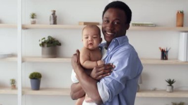 Neşeli bir Afrikalı Amerikalı baba bebeğini parlak ve modern bir yaşam alanına yatırır. Aralarındaki bağ, sevgi, bağlılık ve babalık sevincini vurguluyor..