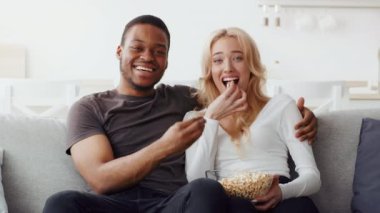 Çift ırklı bir çift rahat bir koltukta oturup birbirlerine gülümserken patlamış mısırlarını paylaşırlar. Rahat atmosferleri, evdeki sıcak akşamlarında sevgi ve şefkat yayıyor..