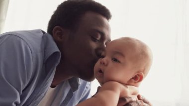 Bir baba bebeğini sıcak bir yuva ortamında özenle ve sevgiyle kucaklar. Aralarındaki bağ sevgi ve neşe saçıyor, çocukluklarının masumiyetini vurguluyor..