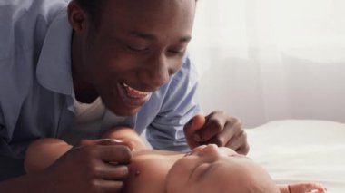 Bir baba bebeğiyle neşe içinde iletişim kurar sevgi ve şefkat dolu derin bir bağ kurar. Sıcak atmosfer, aile bakımının ve birlikteliğin önemini vurgular..