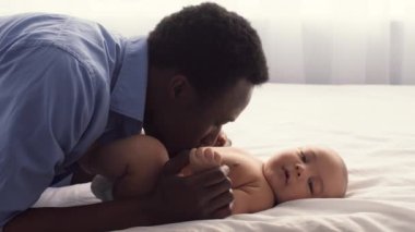 Bir baba bebeğiyle sevgi dolu bir şekilde iletişim kurar, göz teması kurar ve neşeli ifadelerini paylaşır. Sıcak ve davetkar bir evde yataktalar. Bakım ve şefkat dolular..