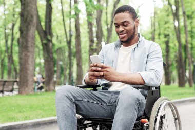 Tekerlekli sandalyedeki genç siyahi adam cep telefonu kullanıyor, parkta mesajları kontrol ediyor, boş yer arıyor. Milenyum Afrikalı Amerikalı adam cep telefonuyla sosyal ağda geziniyor, internette sörf yapıyor.