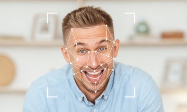 Neşeli bir ifadesi olan bir adam evinde yüz tanıma teknolojisiyle etkileşime geçiyor. Arka planda yenilik ve bağlılık atmosferini geliştiren modern bir dekor yer alıyor..