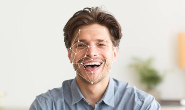 Neşeli bir ifadesi olan bir adam yüz tanıma teknolojisi sergiliyor. Sistem yüzünde geometrik desenler gösteriyor, modern bir ortamda tanımlama sürecini gösteriyor..