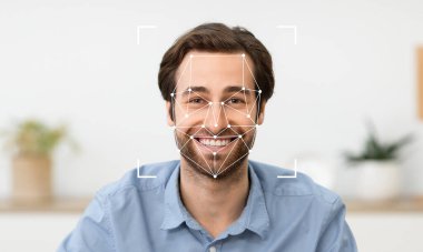 Yüz tanıma teknolojisi özelliklerini incelerken genç bir adam gülümsüyor. Rahat bir ortamda oturuyor. Arka planda yeşillik görünüyor. Bu da sakin bir atmosferi gösteriyor..