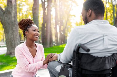 Sevecen siyahi kadın belden aşağısı felçli kocasının elini tutuyor, sonbahar parkında aşkını ifade ediyor. Engelli Afro tekerlekli sandalyedeki adam güz mevsiminde candan karısıyla birlikte dışarıda yürüyor.