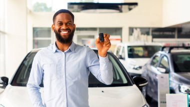 Yeni otomobil. Gülümseyen siyah adam araba anahtarlarıyla lüks aracın yanında poz veriyor, Mutlu Afrikalı Amerikalı erkek müşteri yeni araba satın alımını kutluyor Modern bayilikte, kopyalama alanı