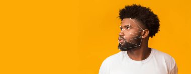 Yüz tanıma sistemi yüzünde belirdiğinde bir adam düşünceli bir şekilde yan tarafa bakar. Parlak turuncu arka plan beyaz gömleğiyle çelişiyor ve sahneye canlılık katıyor..