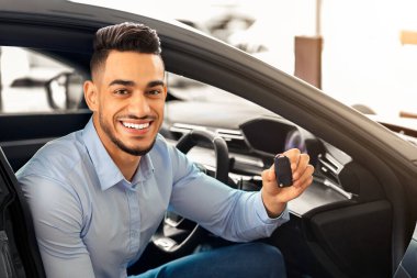 Yakışıklı Arap müşteri arabada oturuyor ve anahtarı tutuyor, kameraya gülümsüyor, galeriden araba alıyor. Neşeli orta doğulu adam güzel bir spor arabanın içinde oturuyor, yeni bir araba aldığına seviniyor.
