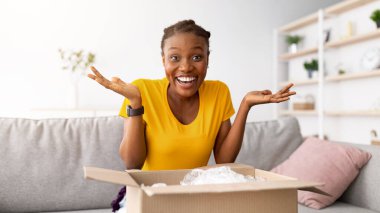 Heyecanlı siyahi kadın paket alıyor, karton kutuları açıyor, büyük alışverişlerle tatmin oluyor. Mutlu Afrikalı Amerikalı kadın, paket açıyor, online teslimattan çok memnun.
