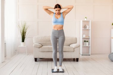 Kilo verme konsepti. Ağırlık tartısı üzerinde duran Şok olmuş Kadın Kafasına Dokunan Kadın Evde Kalan Kilogramlar Aldı. Boş Boşluk