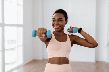 Ağırlıklarla Aile Eğitimi. Dambıllarla egzersiz yapan, vücudunu evde güçlendiren pozitif sporcu kadın. Diş teli takmış, kaslarını çalıştıran, sağlıklı kalan gülümseyen genç bir bayan.