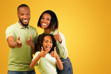 Hey, sen! Heyecanlı siyahi ebeveynler ve kızları kamerayı işaret ediyor, seni seçiyor ve seçiyor, sarı stüdyo arka planında tek başına duruyor, afiş