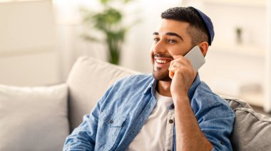 Telefon Çağrısı Konsepti. Arkadaşları ya da ailesi ile akıllı telefonda konuşan rahat bir koltukta oturan gülümseyen genç Yahudi 'nin yakın plan portresi. Boş kopya alanı, seçici odak, bulanık arkaplan