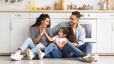 Güzel bir ortadoğu aile babası, anne ve kızı rahat beyaz bir mutfakta yerde oturuyor, sevgi dolu ebeveynler sevimli küçük çocuklarıyla vakit geçiriyorlar, sohbet ediyorlar, gülüyorlar, boşlukları kopyalıyorlar.
