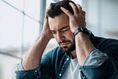 Stres, baş ağrısı, sağlık sorunları, olumsuz duygular. Umutsuz, mutsuz, mutsuz, Avrupalı yakışıklı adam başını tutuyor, acıdan kıvranıyor, arka planda çok çalışıyor ve ağlıyor, kapat.