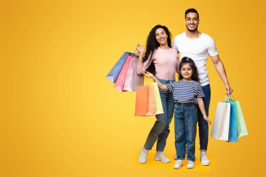 Mevsimlik satışlar. Küçük kızıyla birlikte mutlu bir Arap ailenin portresi bir sürü parlak alışveriş çantası, Orta Doğulu ebeveyn ve çocuk pozu stüdyoda, kopyalama alanı