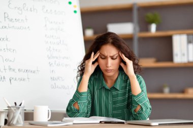 İşten yorgun düştüm. Baş ağrısı çeken, alnına ve şakaklarına dokunan, masa başında oturan, sorunları düşünen yorgun ve stresli genç bir kadının portresi.